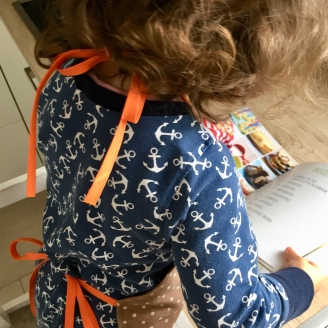 Ein Kind mit blauem Kleid mit weißen Ankern drauf blättert auch durch das Backbuch der kinderleichten Becherküche.
